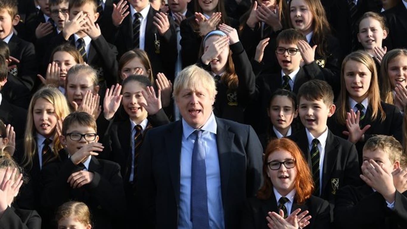 Großbritanniens Premierminister Boris Johnson (M) steht zwischen Schüler bei seinem Besuch eines Colleges.