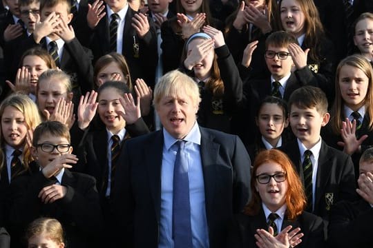 Großbritanniens Premierminister Boris Johnson (M) steht zwischen Schüler bei seinem Besuch eines Colleges.