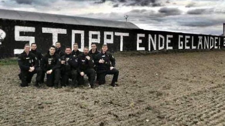 Heikle Aktion: Dieses Foto von neun Polizeibeamten vor einem Graffiti in Brandenburg tauchte im Netz auf – und hat für die Beamten Konsequenzen.