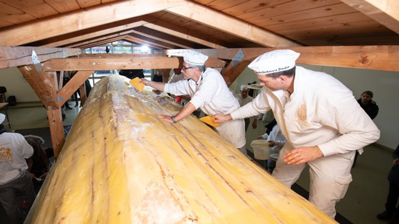 Bäcker der Schutzgemeinschaft Dresdner Stollen streichen Butter und Zucker auf den Riesenstollen.