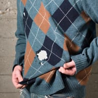 Ein Mann trägt einen Pullover mit Löchern: Viele Schädlinge können im Kleiderschrank großen Schaden anrichten.