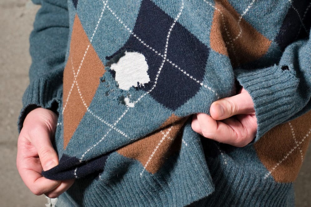 Ein Mann trägt einen Pullover mit Löchern: Viele Schädlinge können im Kleiderschrank großen Schaden anrichten.