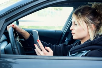 Eine Fahrerin tippt auf ihrem Smartphone: In Australien will die Polizei jetzt Handy-Sünder am Steuer mit Hilfe von intelligenten Kameras ertappen.