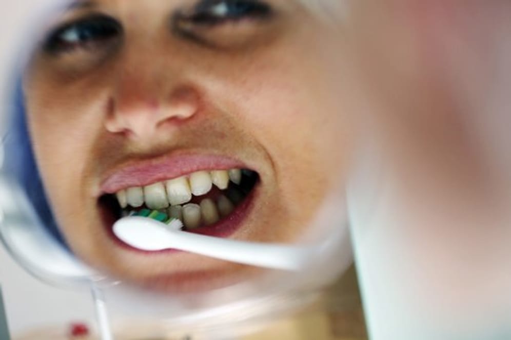 Frau putzt sich die Zähne: Eine vernachlässigte Zahnreinigung kann dazu führen, dass sich im Mund immer mehr Bakterien sammeln. Diese können Entzündungen von Zähnen und Zahnfleisch verursachen, die über Nervenbahnen und Blutgefäße auch in den Körper gelangen.