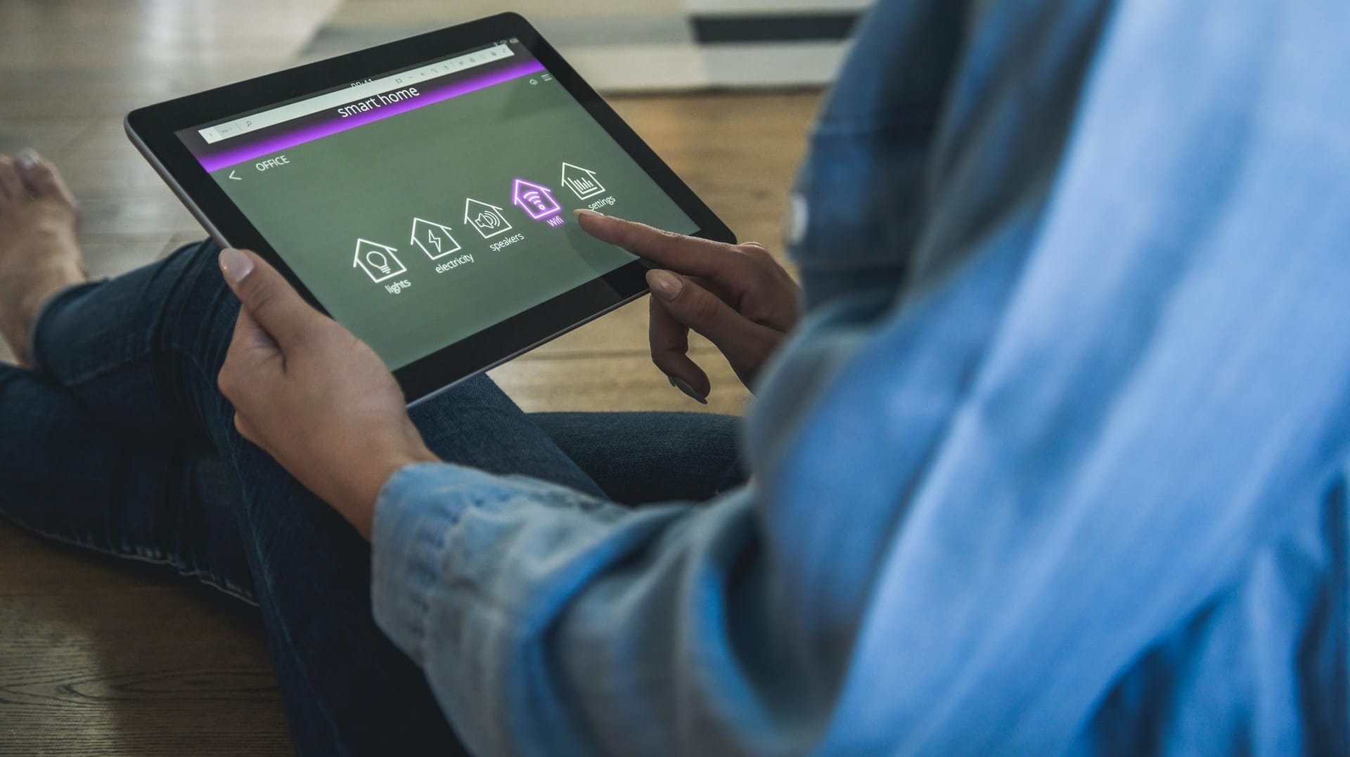 Eine Person sitzt auf dem Boden und steuert das smarte Zuhause vom Tablet aus: Es kann praktisch sein, alle Heimgeräte mit dem Internet zu verbinden – aber auch gefährlich.