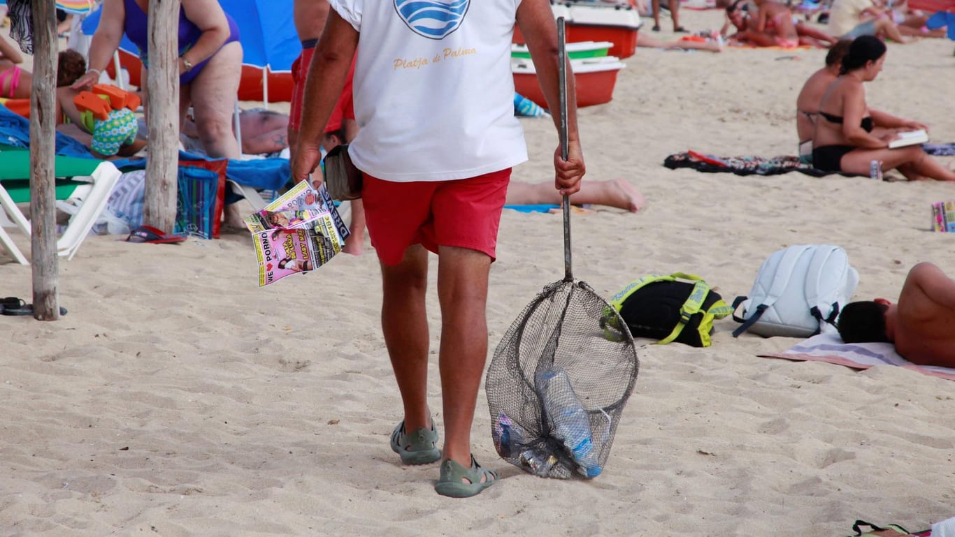 Ein Mann sammelt Müll am Strand von Palma de Mallorca ein.