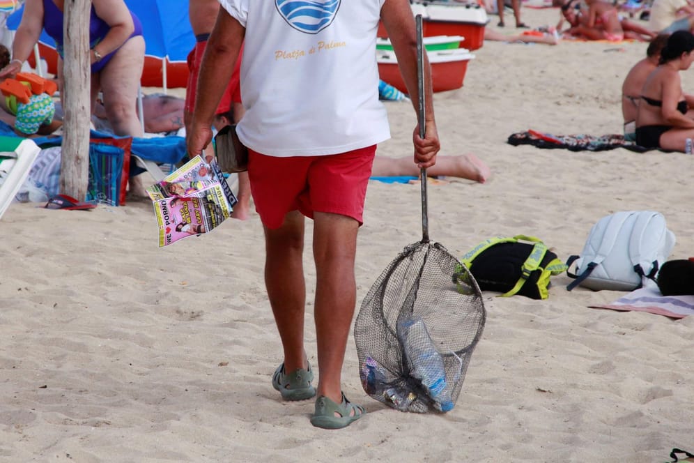 Ein Mann sammelt Müll am Strand von Palma de Mallorca ein.