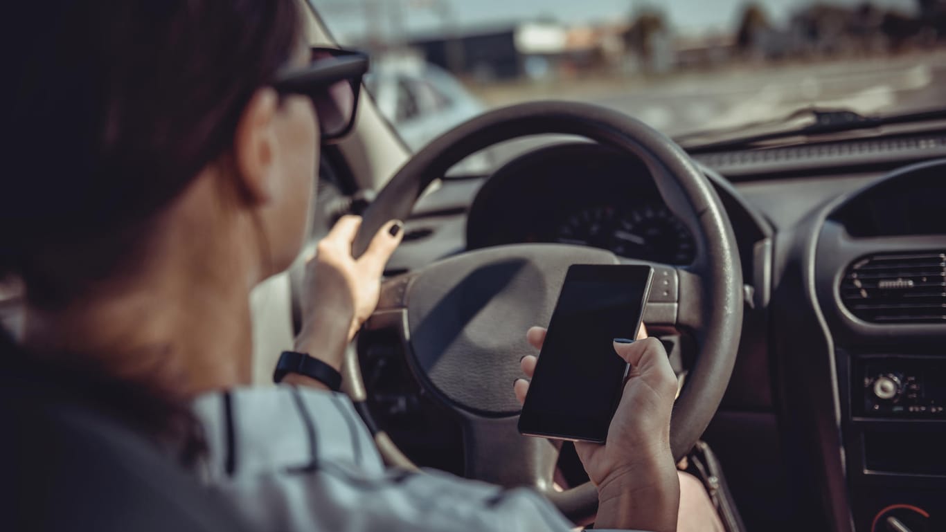 Eine Frau im Auto mit Handy in der Hand: Selbst am Steuer können viele Fahrer auf ihre elektronischen Geräte nicht verzichten.