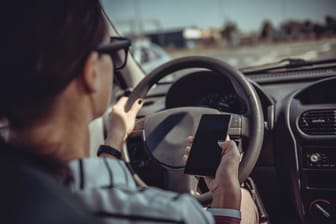 Eine Frau im Auto mit Handy in der Hand: Selbst am Steuer können viele Fahrer auf ihre elektronischen Geräte nicht verzichten.