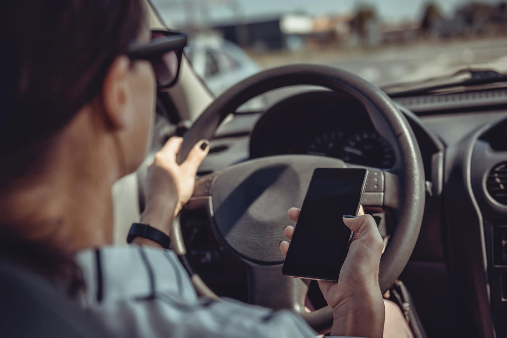 Eine Frau im Auto mit Handy in der Hand: Selbst am Steuer können viele Fahrer auf ihre elektronischen Geräte nicht verzichten.