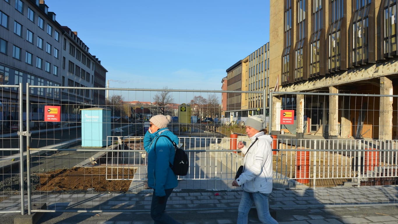 Menschen gehen an einem Bauzaun vorbei: In der Kieler Innenstadt wird ein Kanal gebaut.