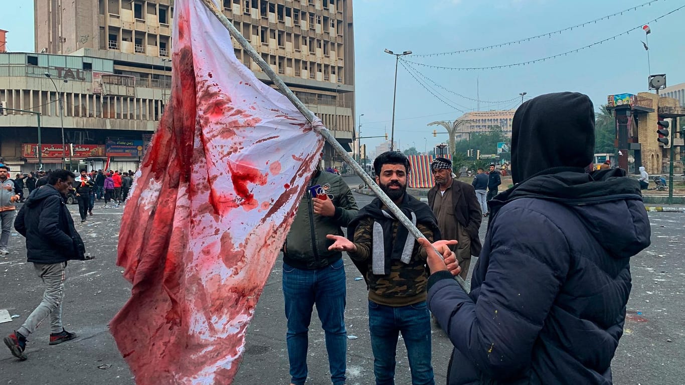 Ein Mann hält eine blutbefleckte Flagge hoch: Wer für die Angriffe in der Nähe des größten Protestcamps in Bagdad verantwortlich ist, ist unklar.