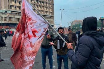 Ein Mann hält eine blutbefleckte Flagge hoch: Wer für die Angriffe in der Nähe des größten Protestcamps in Bagdad verantwortlich ist, ist unklar.