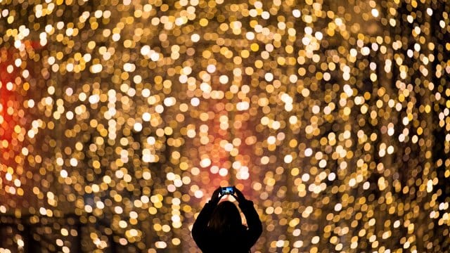 Eine Frau fotografiert die Fassade eines mit Lichterketten weihnachtlich geschmückten Einkaufszentrums. Eine Frau fotografiert die Fassade eines mit Lichterketten weihnachtlich geschmückten Einkaufszentrums.
