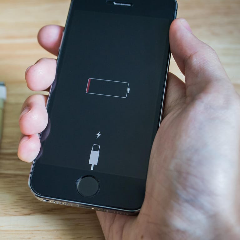 Ein Nutzer hält ein iPhone, dessen Akku fast leer ist: Wenn das Smartphone zu viel Energie verbraucht, kann das verschiedene Gründe haben.