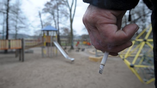 Ein Mann hält auf einem Spielplatz eine Zigarette in der Hand.