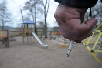 Ein Mann hält auf einem Spielplatz eine Zigarette in der Hand.