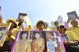 Gratulanten sitzten mit Bildern von Thailands König Maha Vajiralongkorn und Königin Suthida vor dem Großen Palast.