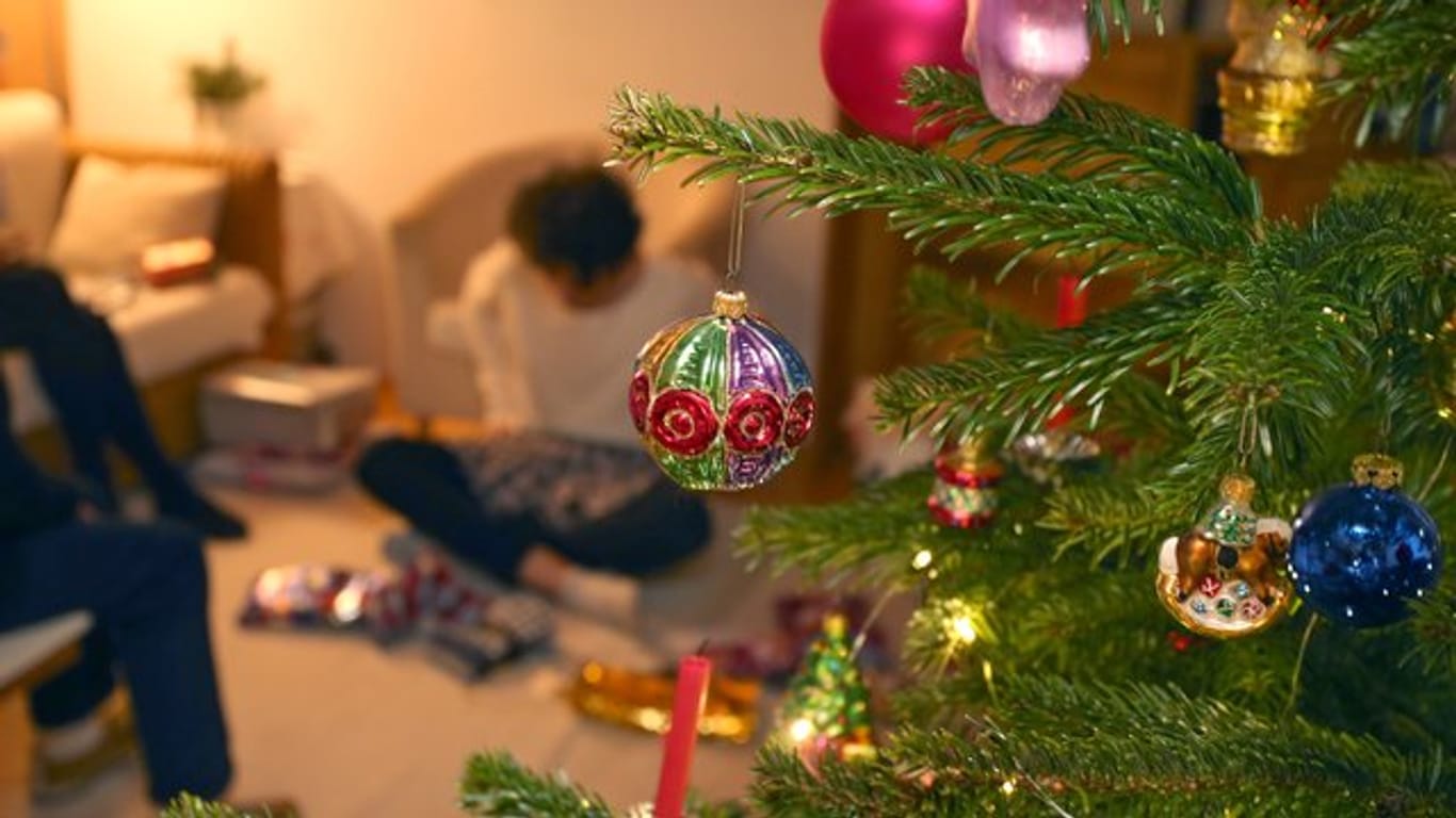 Eine Junge packt hinter einem geschmücktem Christbaum Weihnachtsgeschenke aus.