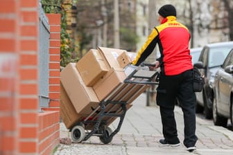 Ein DHL-Mitarbeiter schiebt Pakete: Hohe Investitionen der Paketbranche sollen dazu führen, dass Empfänger zukünftig genau wissen, wann der Paketbote da sein wird.