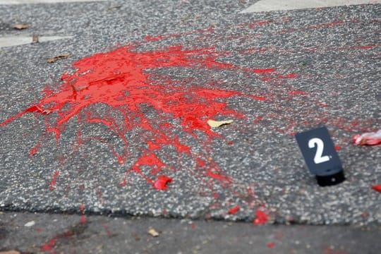 Farbe und Glasscherben liegen auf einer Straße hinter einer Polizeiabsperrung.