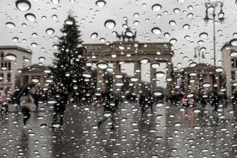 Grauer Himmel in Berlin: Das Brandenburger Tor und ein Weihnachtsbaum stehen hinter der Scheibe eines Autofensters auf dem Regentropfen hängen.