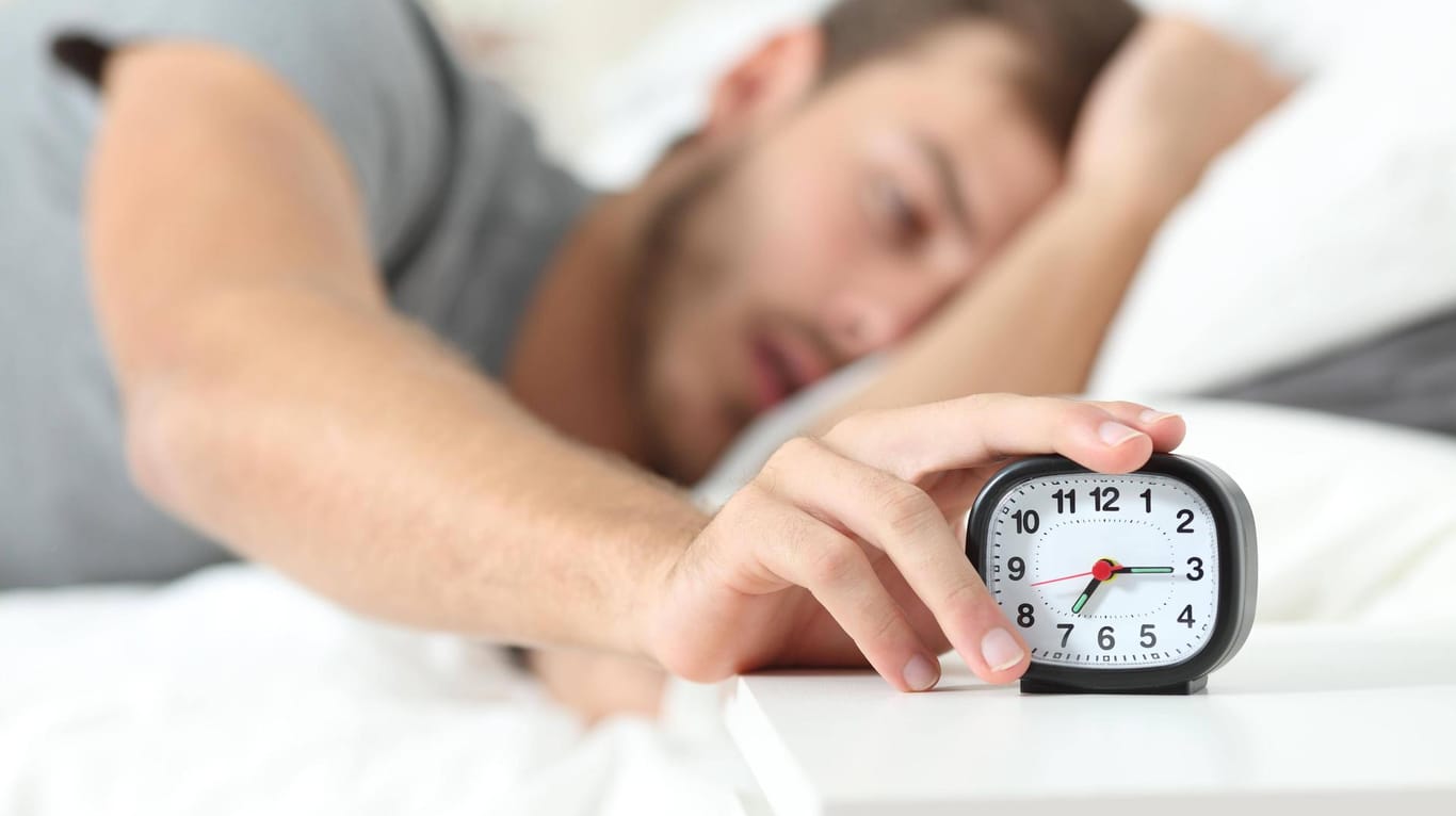Mann stellt Wecker aus: Im Winter schlafen Menschen länger, aber schlechter – und sind dann tagsüber müder als im Sommer.