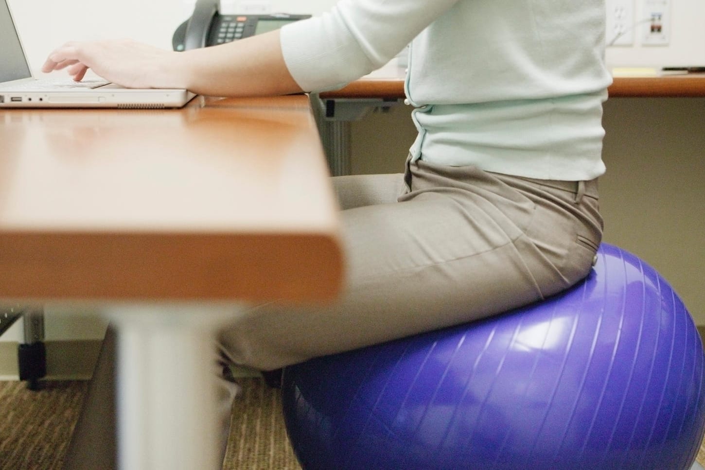 Eine Frau sitzt auf einem Gymnastikball: Ein verstellbarer Bürostuhl hat dem Ball gegenüber mehr Vort- als Nachteile.