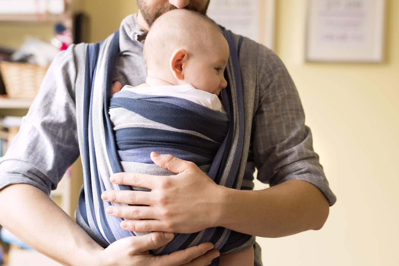 Ein Mann hält ein Baby im Tragetuch: Stiftung Warentest hat 15 Produkte angeschaut – darunter Tragetücher, Halbschnallen- und Vollschnallen-Tragen.