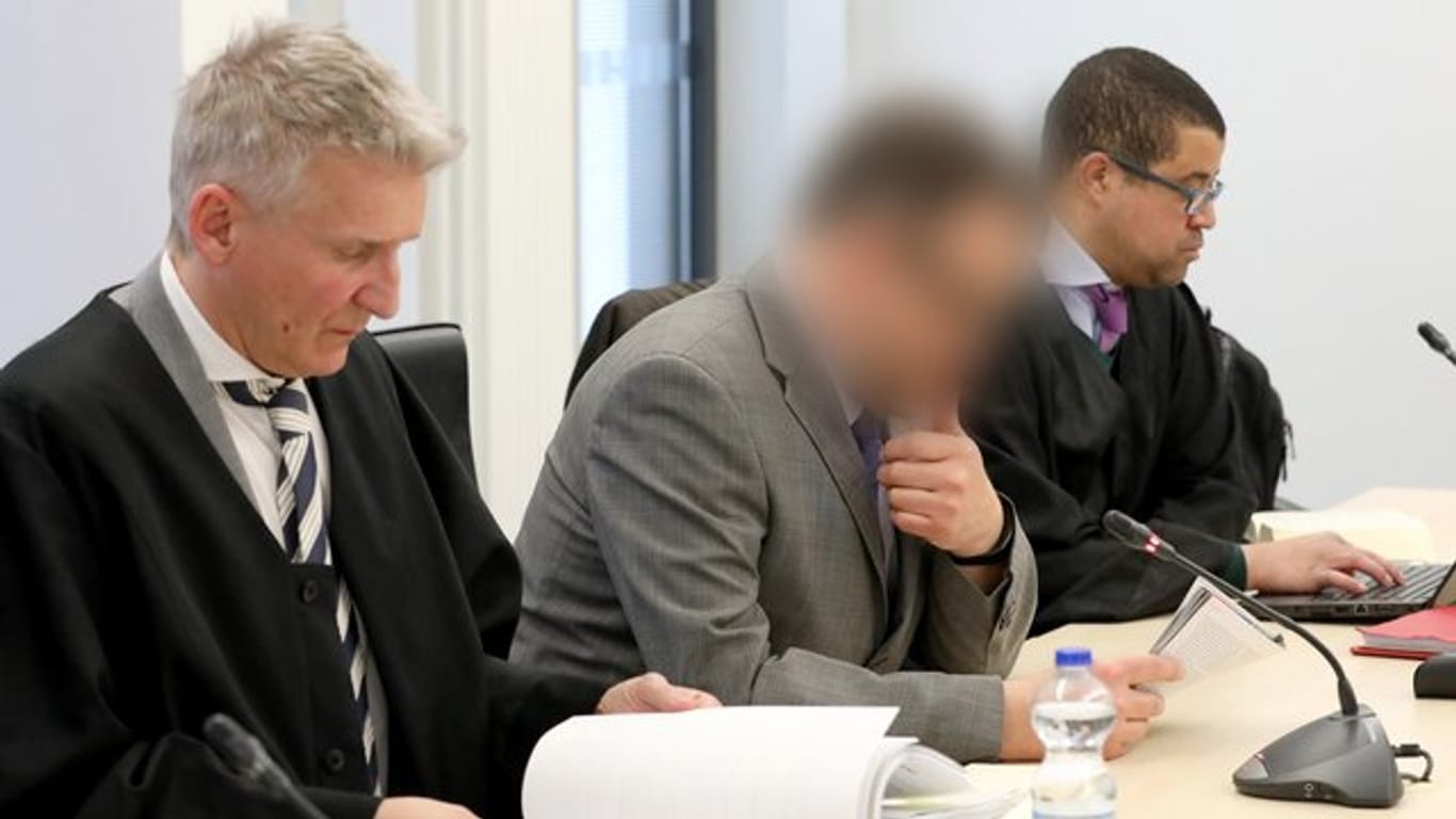 Der angeklagte Neurochirurg (M) mit seinen Anwälten im Rostocker Landgericht.