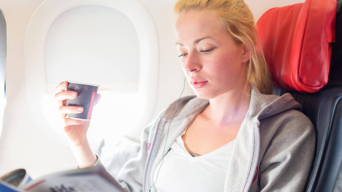 Eine Frau liest im Flugzeug und hält einen Kaffee in der Hand: Wer haftet bei Verbrühungen im Flugzeug?