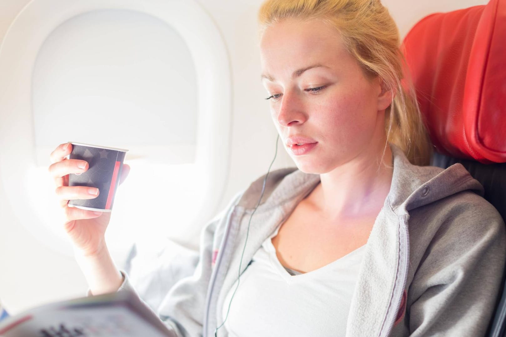 Eine Frau liest im Flugzeug und hält einen Kaffee in der Hand: Wer haftet bei Verbrühungen im Flugzeug? Eine Frau liest im Flugzeug und hält einen Kaffee in der Hand: Wer haftet bei Verbrühungen im Flugzeug?