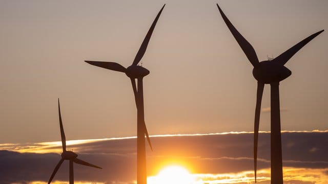 Die Sonne geht hinter Windkraftanlagen unter.