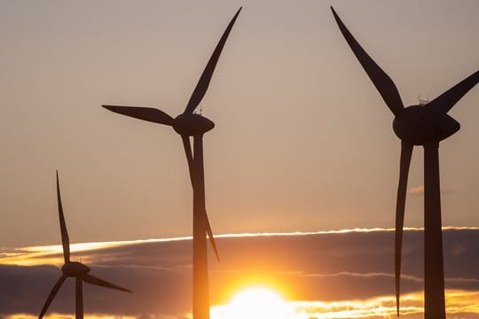 Die Sonne geht hinter Windkraftanlagen unter.