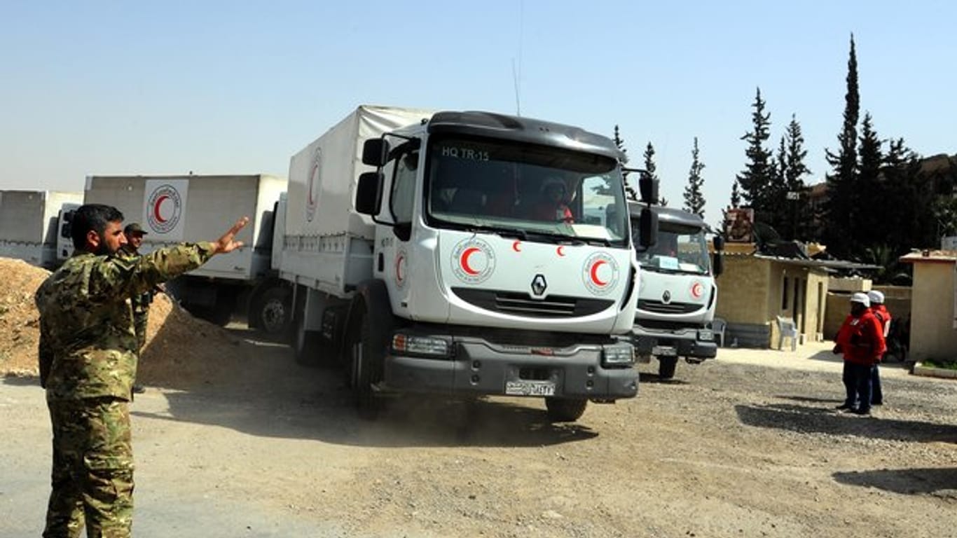 Ein syrischer Soldat weist Lastwagen des Syrisch-Arabischen Roten Halbmondes mit Hilfsgütern in Richtung eines umkämpften Gebiets (Archiv).