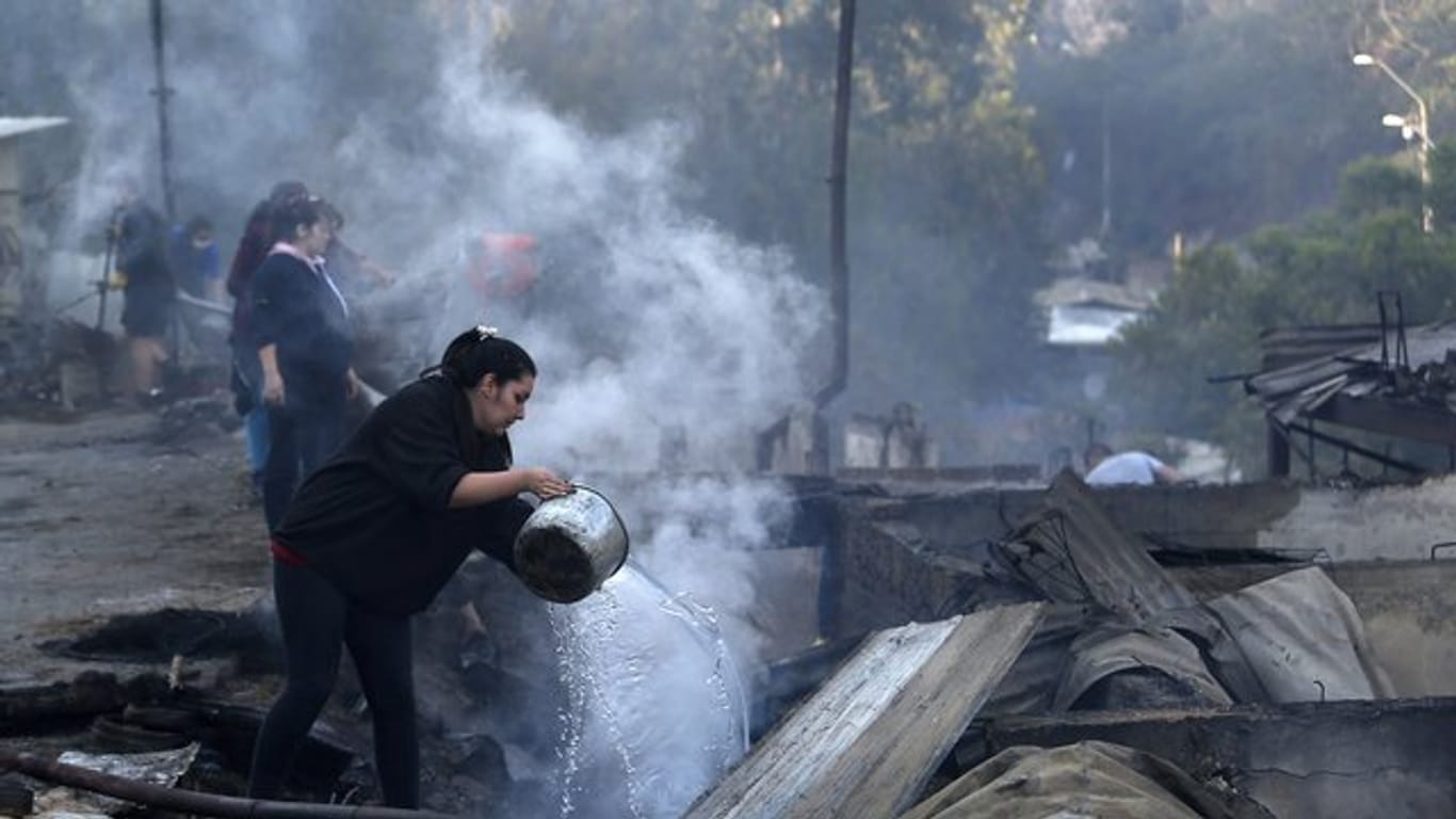 Einwohner schütten Wasser auf die qualmenden Überreste ihrer Häuser, die bei einem Brand zerstört wurden.