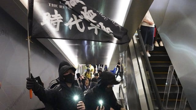 Demonstranten mit Mundschutz tragen eine Flagge mit der Aufschrift "Befreit Hongkong, die Revolution unserer Zeit" in einem Einkaufszentrum.