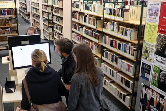 Besucher einer Stadtbibliothek informieren sich an einem Computer.