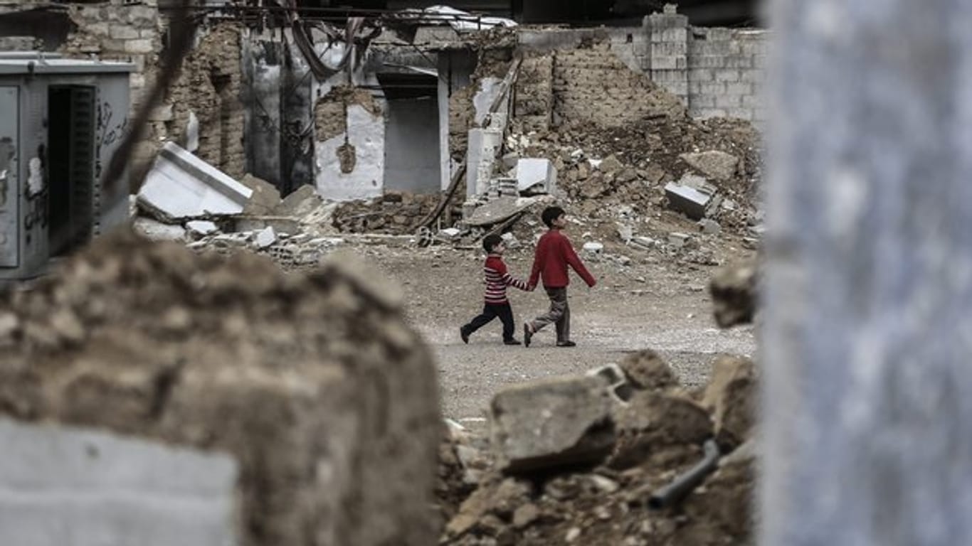 Zwei syrische Jungen gehen Hand in Hand an zerstörten Häusern vorbei.