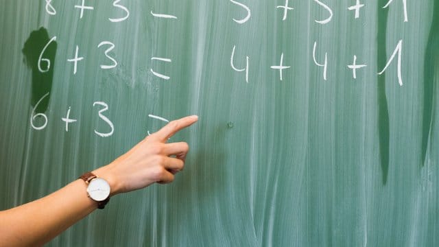 Eine Lehrerin schreibt in einer Schule Rechenaufgaben an eine Tafel. Eine Lehrerin schreibt in einer Schule Rechenaufgaben an eine Tafel.