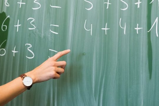 Eine Lehrerin schreibt in einer Schule Rechenaufgaben an eine Tafel.