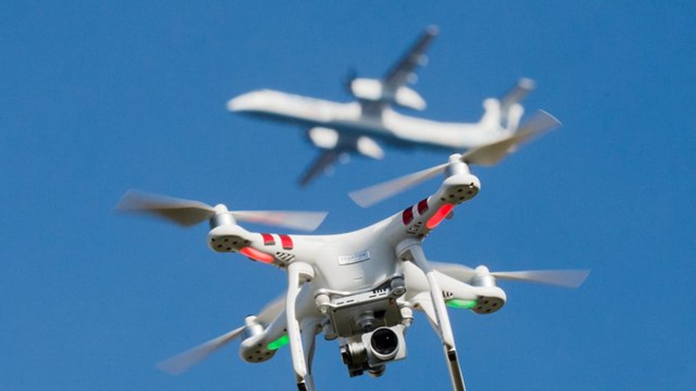 Eine private Drohne fliegt in knapp 10 Metern Flughöhe über einem Garten, in weiter Entfernung ist ein Flugzeug beim Anflug auf den Flughafen Düsseldorf zu sehen ist.