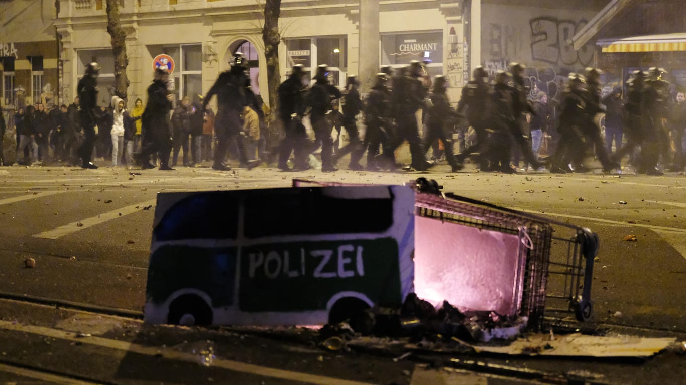 Polizisten räumen eine Kreuzung im Stadtteil Connewitz, während im Vordergrund ein Einkaufswagen liegt.