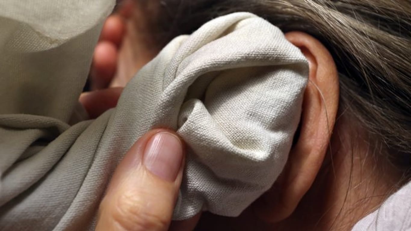 Eine Frau hält sich ein Zwiebelsäckchen, ein Tuch mit geschnittenen Zwiebeln, an ihr Ohr.