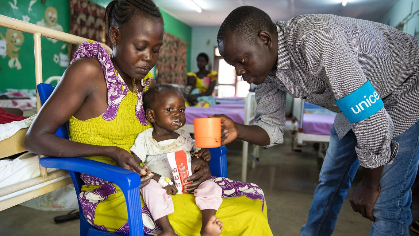 Ein Gesundheitshelfer von Unicef gibt Sony (16 Monate) einen Becher mit Wasser. Sony ist mangelernährt und wird mit Erdnusspaste behandelt.