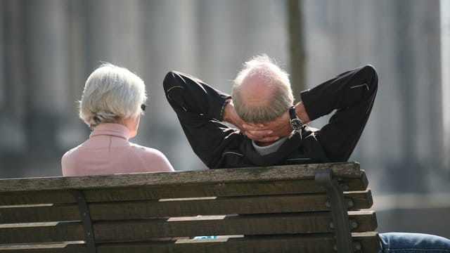 Ein Rentnerpaar sitzt auf einer Bank und sonnt sich.