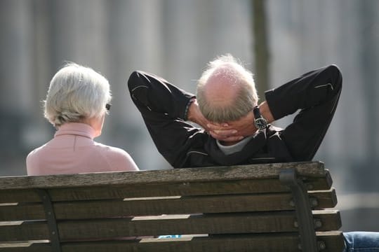 Ein Rentnerpaar sitzt auf einer Bank und sonnt sich.