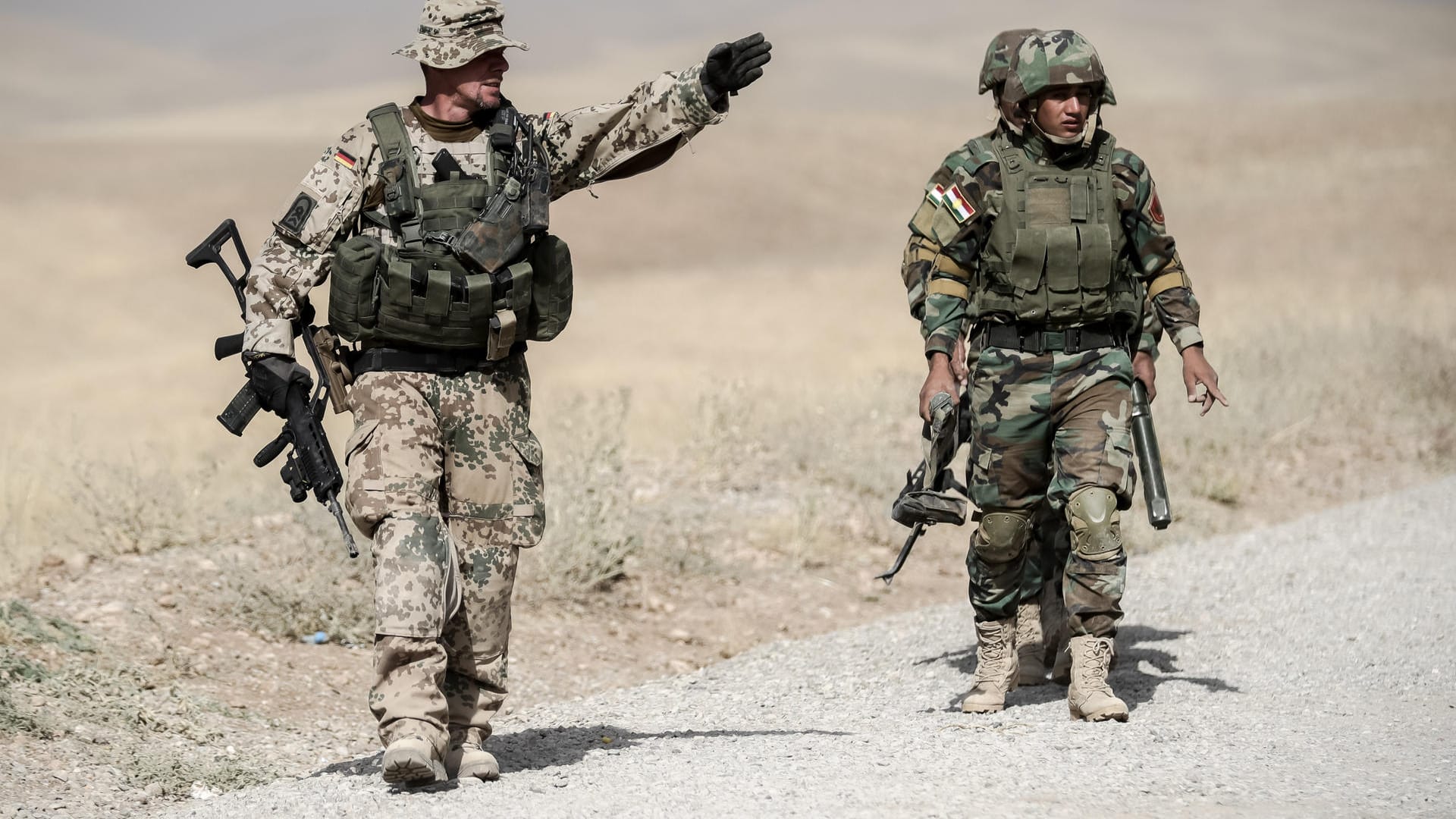 Irak, Erbil (Archivbild): Bundeswehrsoldaten und kurdische Peshmerga Soldaten gehen in der Ausbildungseinrichtung Bnaslawa bei einer Übung am Rand einer Straße entlang.