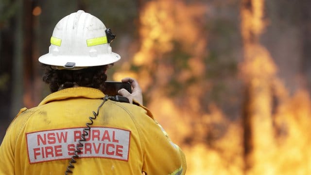 Ein Feuerwehrmann fotografiert mit seinem Smartphone eines der Buschfeuer bei Tomerong.