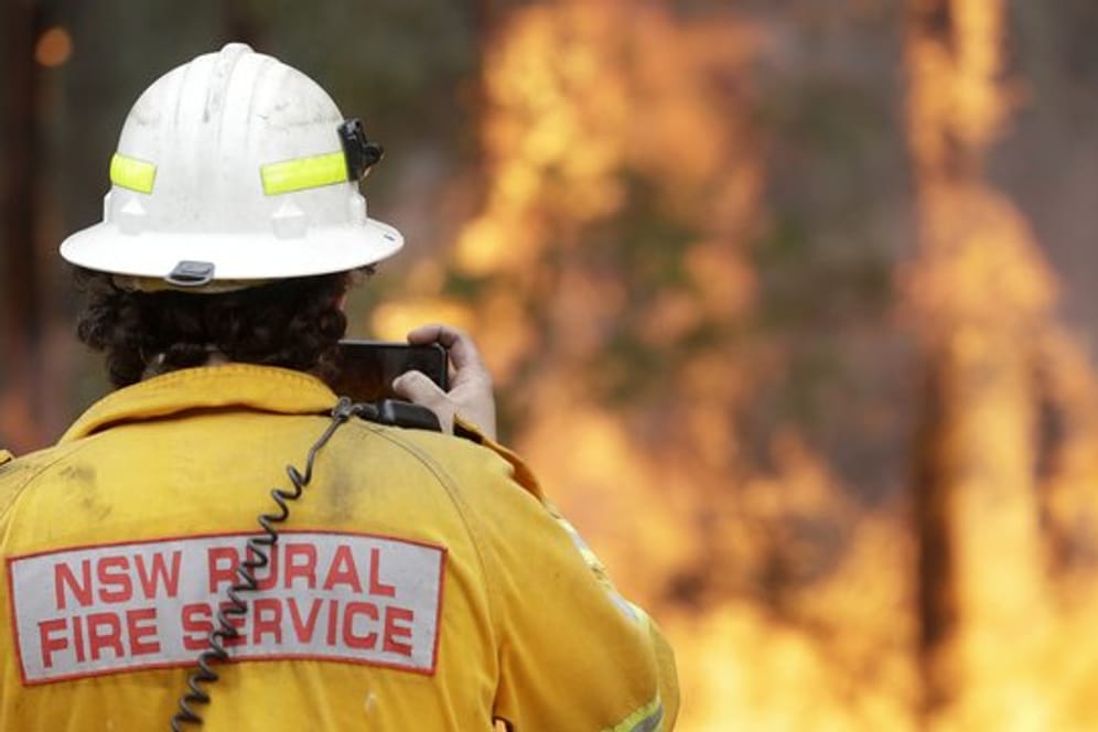 Ein Feuerwehrmann fotografiert mit seinem Smartphone eines der Buschfeuer bei Tomerong.